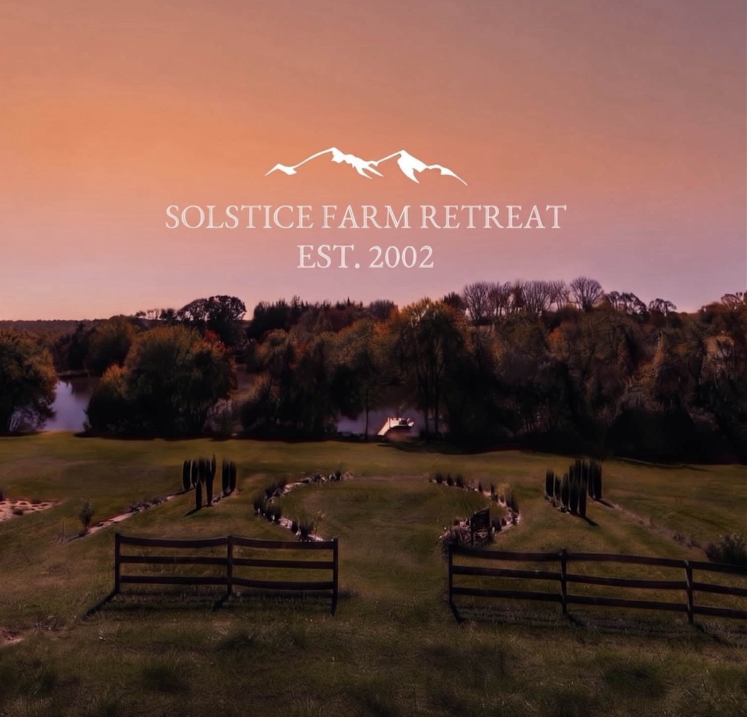 Solstice Farm Retreat at dusk: the lawn running down to the pond and dock, with the logo set against an orange and violet sky